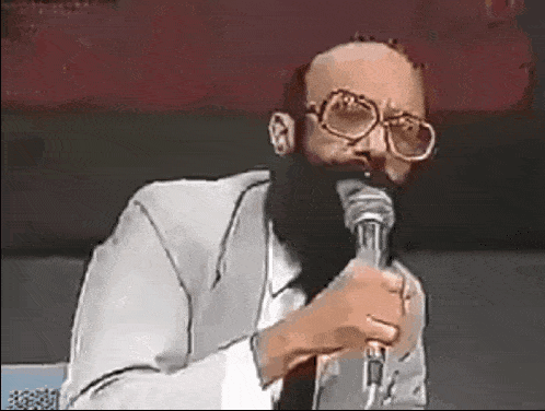 a bald man with glasses and a beard is holding a microphone