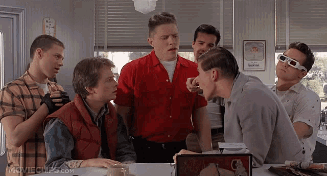 a group of men are gathered around a table with a moviechips.com logo on the bottom