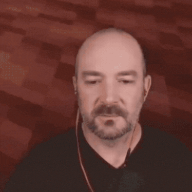 a bald man with a beard wearing earbuds and a ring on his finger