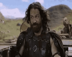 a man with long hair and a beard is sitting in a car in a field .
