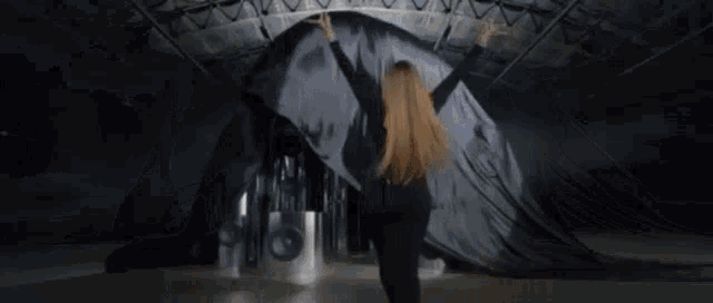 a woman in a black dress is standing in front of a large black object with her arms outstretched