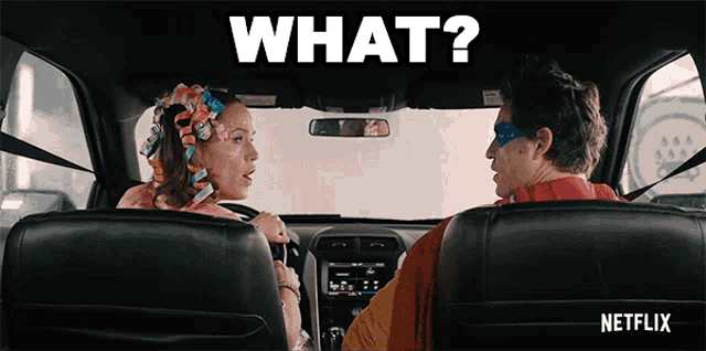 a man in a superhero costume is driving a car with a woman in curlers behind him .