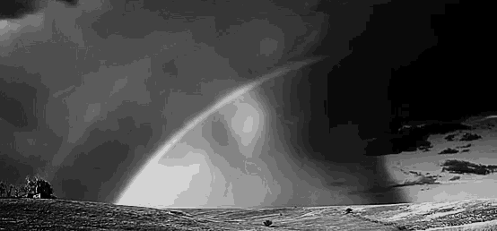 a black and white photo of a rainbow over a hill