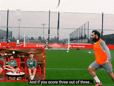 a man in an orange vest kicks a soccer ball on a field