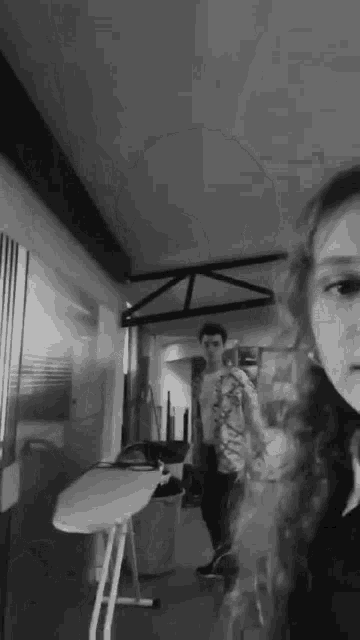 a man and a woman are standing in a room with an ironing board .