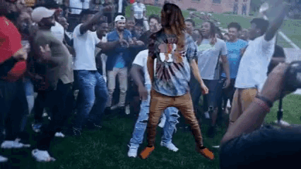 a man is dancing in front of a crowd of people on a field .