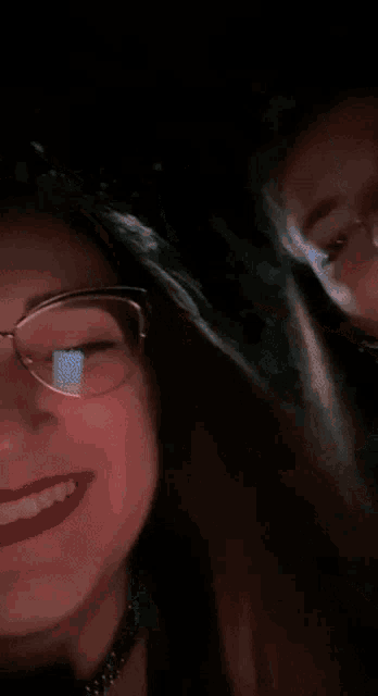a woman with glasses and red lipstick is smiling next to another woman
