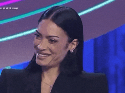 a woman wearing a black jacket and earrings is smiling and waving