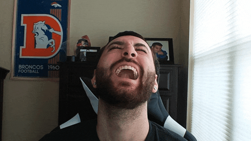 a man laughs in front of a poster for the broncos football team