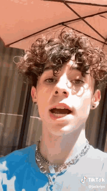 a young man with curly hair wearing a blue shirt and a chain around his neck .