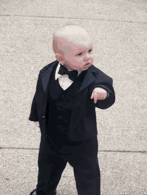 a baby wearing a tuxedo and bow tie points at something