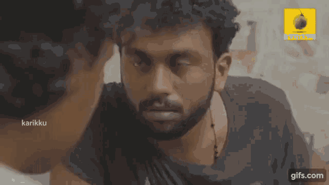 a man with a beard is talking to another man with a sticker on his shirt that says karikku
