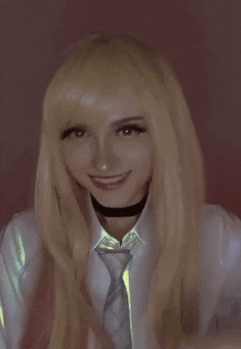 a girl with blonde hair and a tie is smiling and giving a peace sign