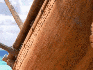 a close up of a wooden boat on the beach with the ocean in the background