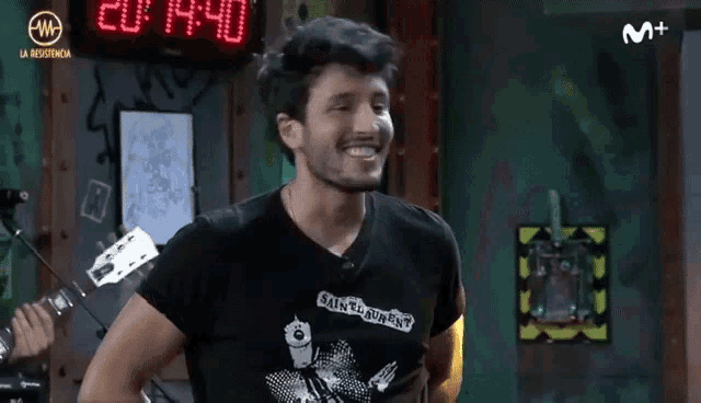 a man wearing a saint laurent t-shirt smiles in front of a m + sign