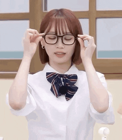 a girl wearing glasses and a school uniform is adjusting her glasses .