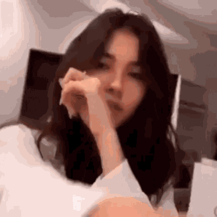 a girl with long dark hair is sitting in a chair with her hand on her chin .