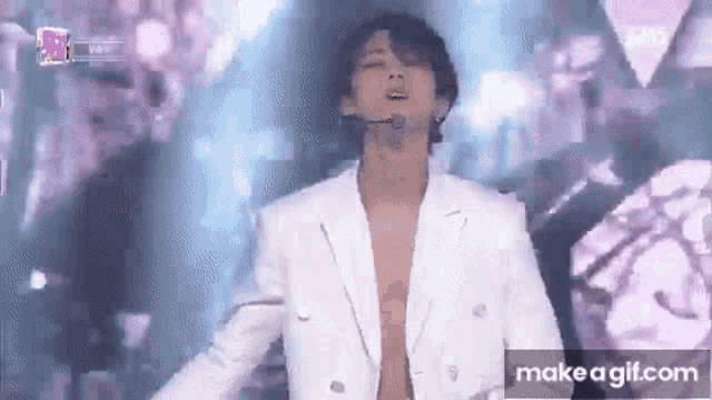 a man is standing on a stage without a shirt on and singing into a microphone .