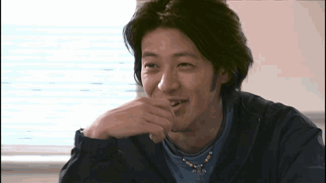 a man wearing a blue shirt and a necklace with a cross on it smiles