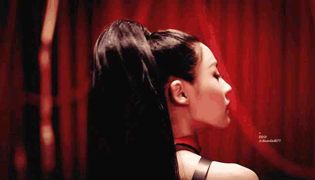 a close up of a woman 's face with a red curtain behind her and the letters ddd on the bottom right