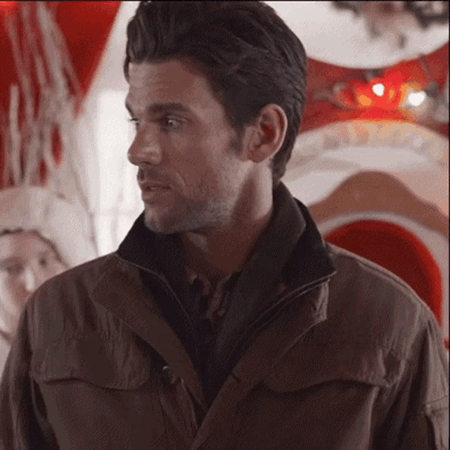 a man in a brown jacket is standing in front of a christmas decoration
