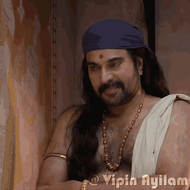 a man with long hair and a beard is wearing a blue headband with a red dot on the forehead