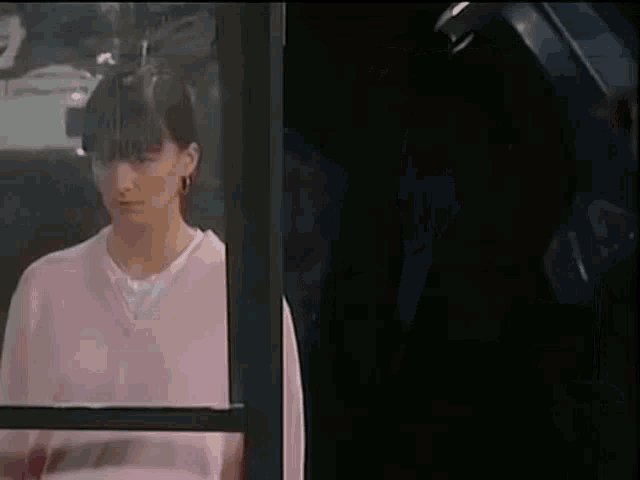 a woman in a pink sweater is standing in front of a window .