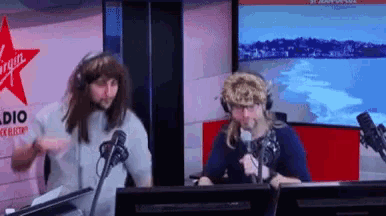 two men are dancing in front of microphones in front of a virgin radio sign