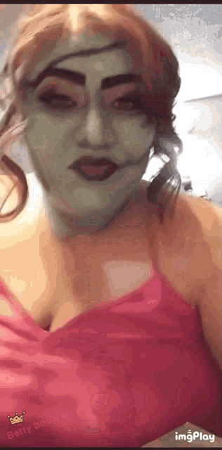 a woman with green paint on her face is wearing a pink top .