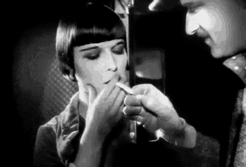 a woman is lighting a cigarette in a black and white photo while a man looks on .