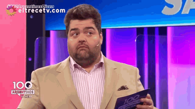 a man in a tan suit holds a 100 argentinas video in his hand