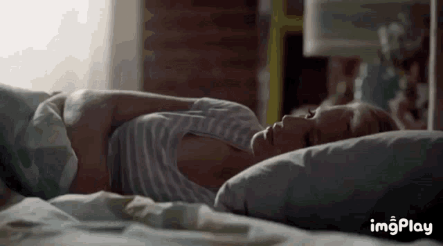 a woman is laying in bed with her head on a pillow and her arms around her stomach .