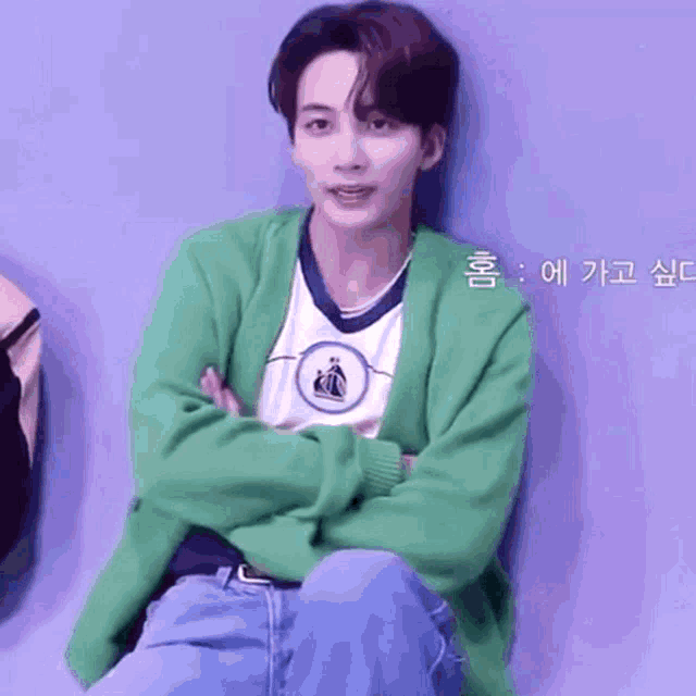 a young man in a green sweater is sitting with his arms crossed
