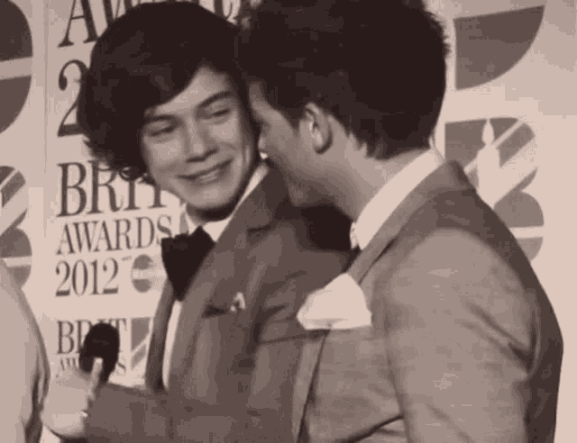 two men are standing in front of a brit awards 2012 sign