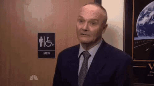 a man in a suit and tie is standing in front of a handicapped men 's bathroom .