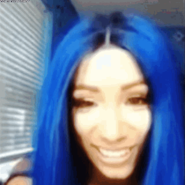 a woman with blue hair is smiling and looking at the camera in a blurry photo .