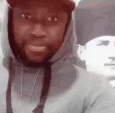 a man wearing a hoodie and a hat is smiling in front of a blurry picture of another man .