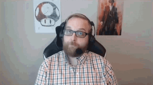 a man with a beard and glasses is wearing headphones and a microphone while sitting in a chair .