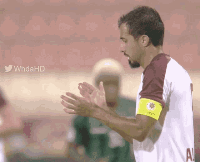 a soccer player applauds while wearing a yellow armband that says al