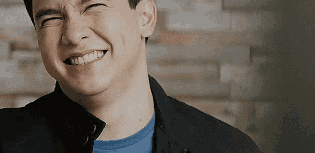 a man wearing a black jacket and a blue shirt is smiling with his eyes closed