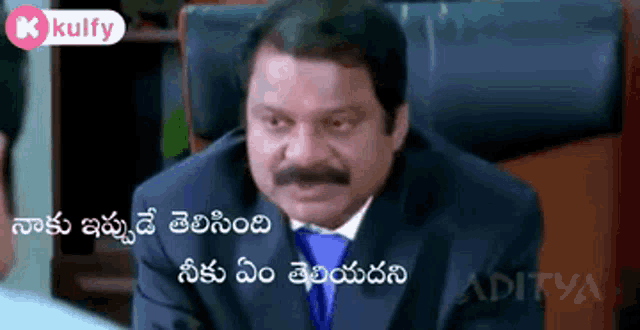 a man in a suit and tie is sitting in a chair with a caption in telugu .