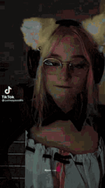 a girl with pink hair and glasses is wearing a cat ear headband .