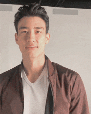a man wearing a white shirt and a brown jacket smiles for the camera