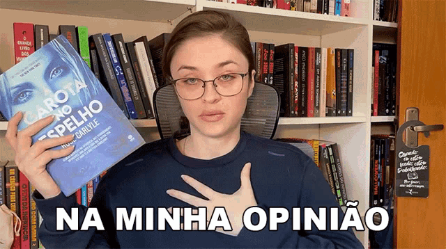 a woman is holding a book in front of a bookshelf and says na minha opiniao