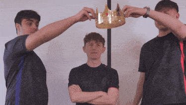 a man in a black shirt is holding a crown over another man 's head