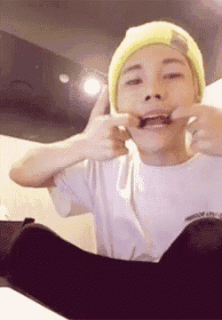 a young man wearing a yellow beanie and a white t-shirt making a funny face