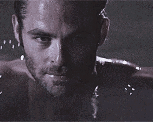 a man with a beard is taking a bath and looking at the camera with water splashing on his face .