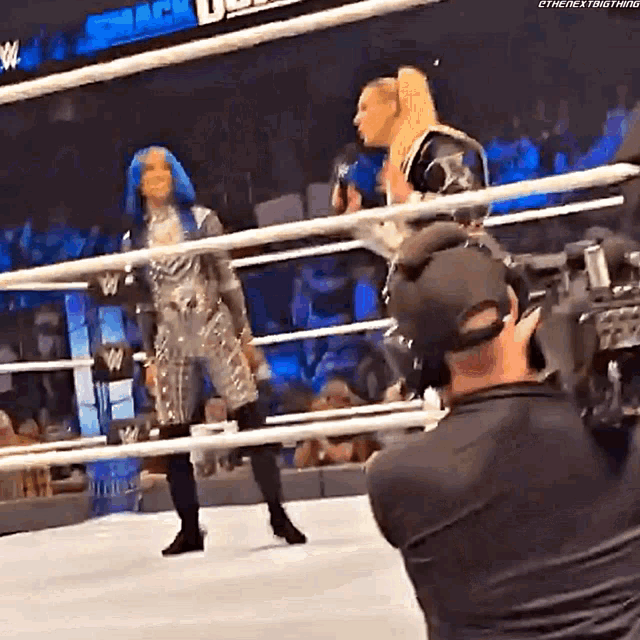 two women are standing in a wrestling ring while a cameraman takes a picture .