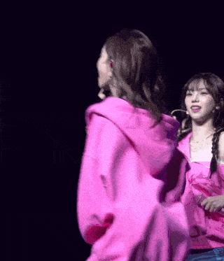 a woman in a pink hoodie stands next to another woman on a stage