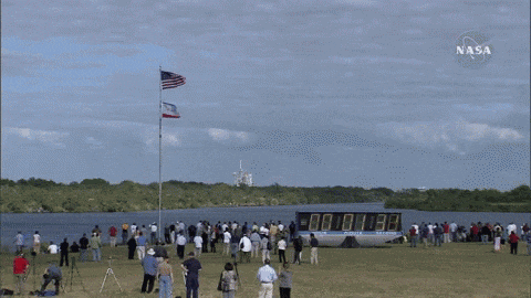 a crowd of people gathered in a field with a nasa logo in the background